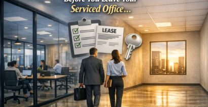 Two people walk down an office corridor carrying folders and a suitcase, with lease documents and keys illustrated above, signalling the process of leaving a serviced office. Office workers are visible through glass walls. Text reads "Before You Leave Your Serviced Office...