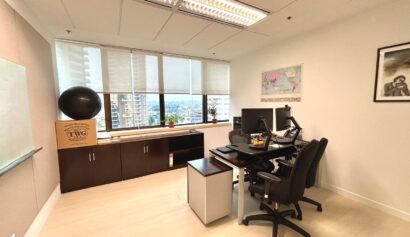 Modern office with two chairs, a desk with computer monitors, large windows with city view, a filing cabinet, and wall decorations including a map and a framed photograph.