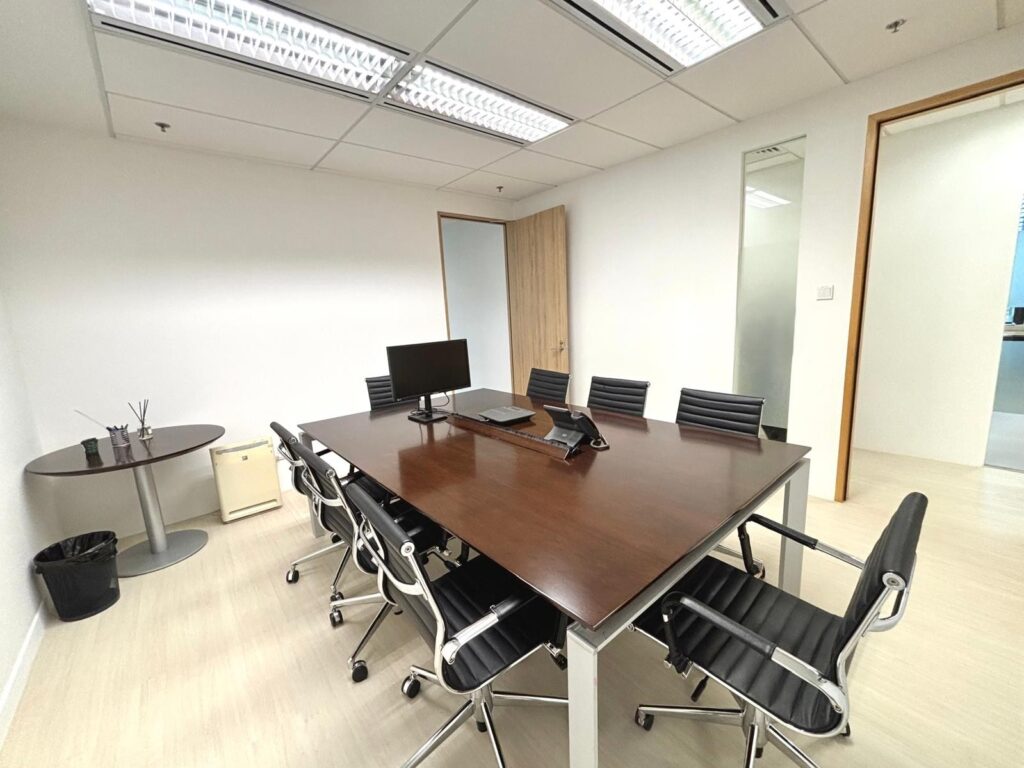 A modern conference room with a large wooden table, eight black chairs, a computer monitor, conference telephone, and minimal decor.
