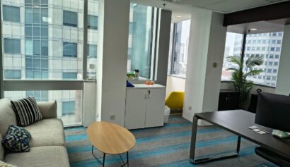 Modern office with large windows, a sofa, round coffee table, desk, cupboard, and a small yellow chair in a corner nook.
