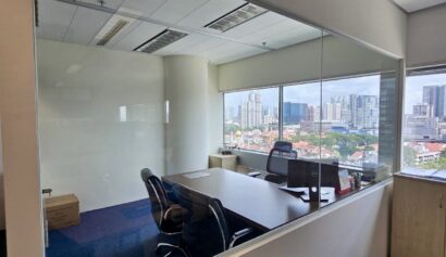 Glass-walled office with two chairs, a desk, a whiteboard, and a city skyline visible through the window.