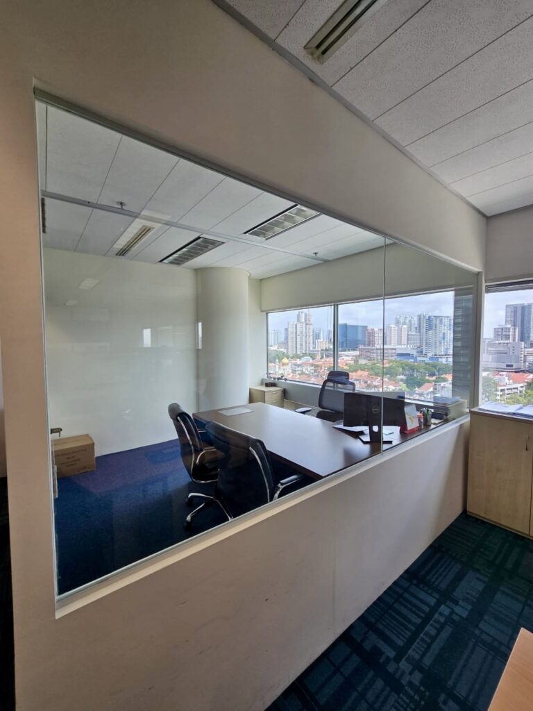 Glass-walled office with two chairs, a desk, a whiteboard, and a city skyline visible through the window.