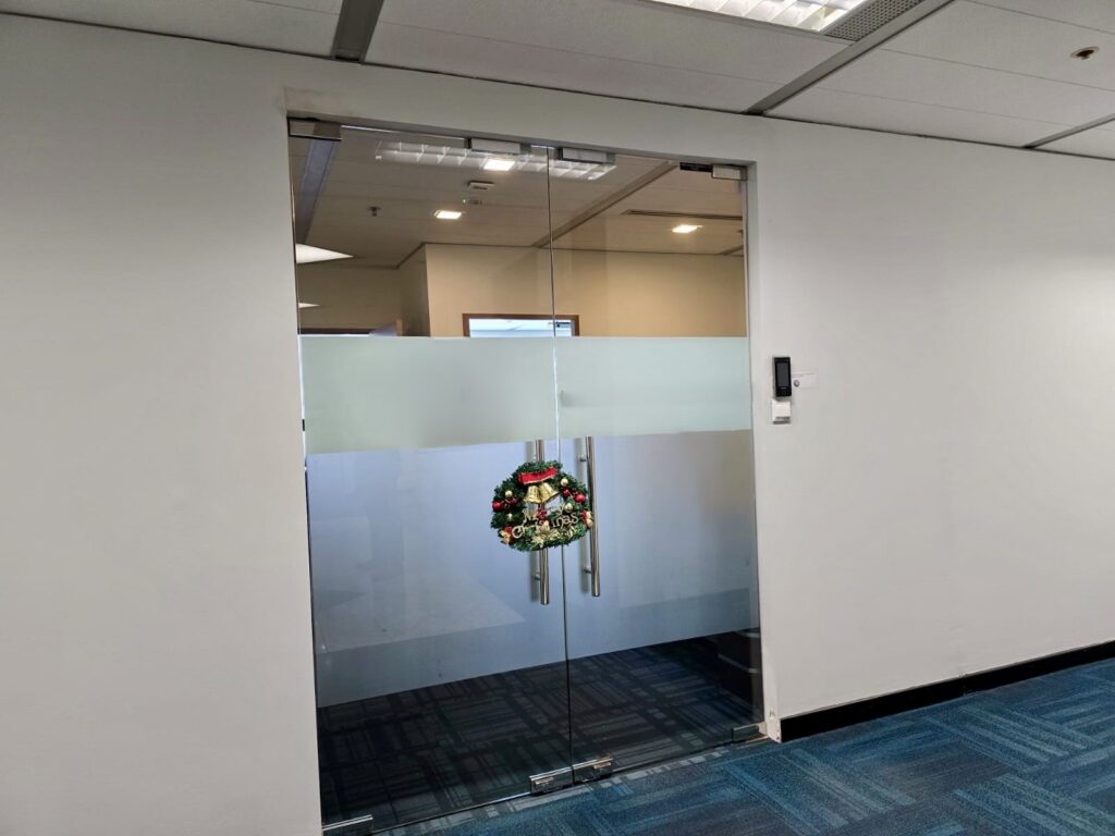 Glass office doors with a frosted stripe and a holiday wreath hanging at the centre. Blue carpeted floor and white walls are visible.