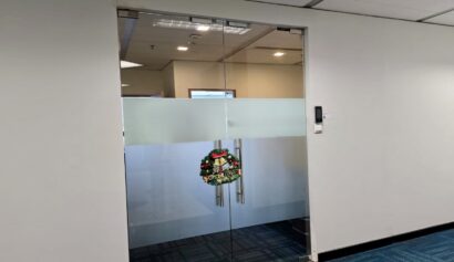 Glass office doors with a frosted stripe and a holiday wreath hanging at the centre. Blue carpeted floor and white walls are visible.