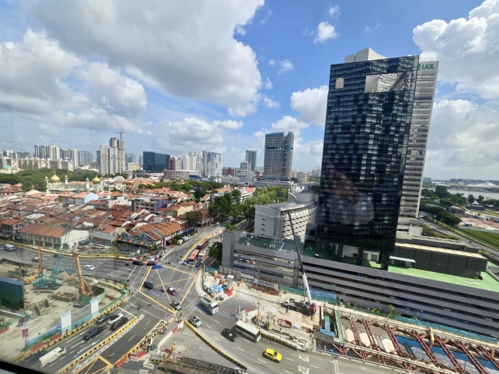 A cityscape showing a mix of tall modern buildings, older low-rise structures, busy roads, and ongoing construction under a partly cloudy sky.