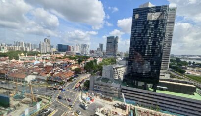 A cityscape showing a mix of tall modern buildings, older low-rise structures, busy roads, and ongoing construction under a partly cloudy sky.
