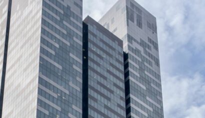 A modern high-rise building with a glass façade featuring a geometric pattern, set against a partly cloudy sky.