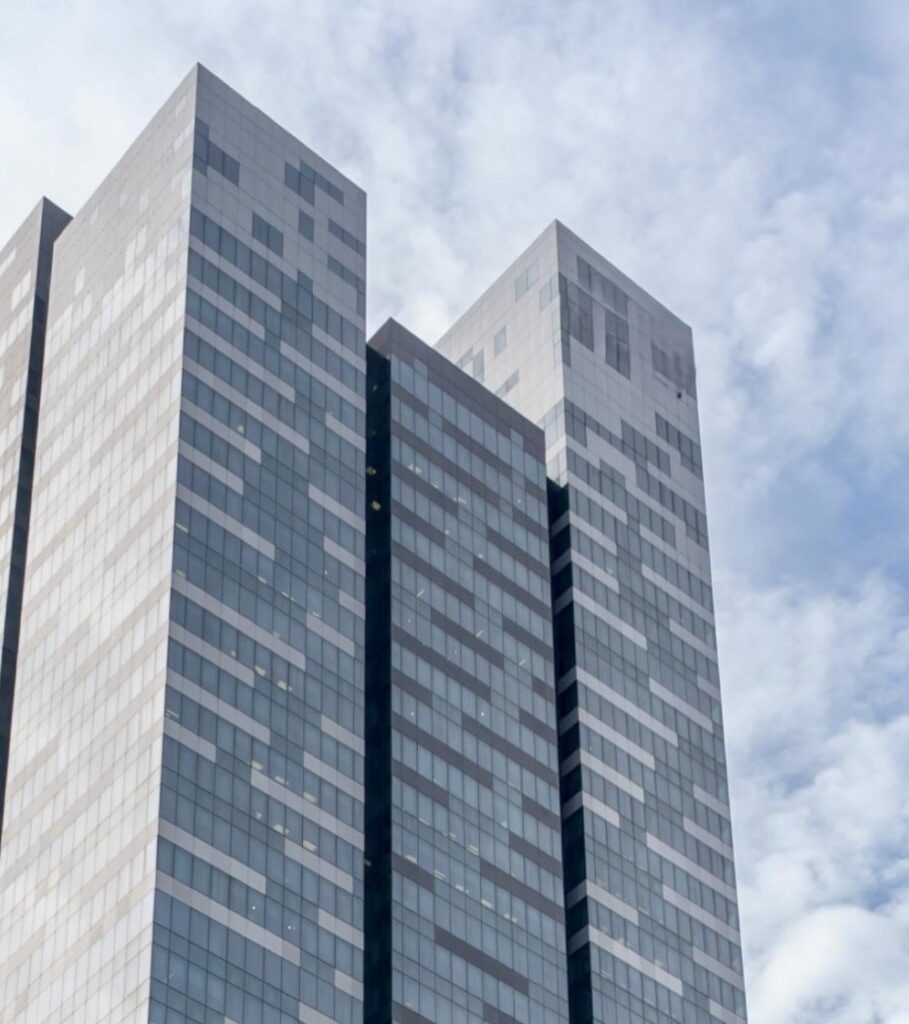 A modern high-rise building with a glass façade featuring a geometric pattern, set against a partly cloudy sky.