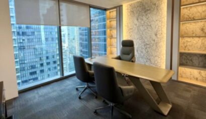Modern office with a wooden desk, three chairs, large windows showing city buildings, and illuminated wall shelves.