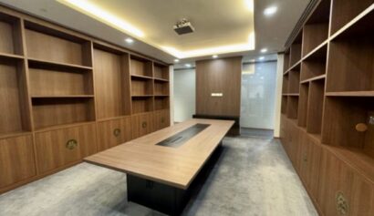 Modern conference room with built-in wooden shelves, a long table at the centre, recessed lighting, and carpeted floor.