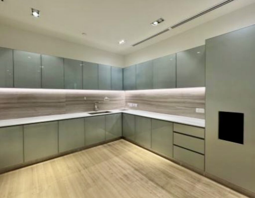 Modern kitchen with light wood flooring, grey cupboards, white worktops, and under-cupboard lighting. The space is clean, uncluttered, and features a minimalist design.