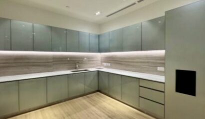 Modern kitchen with light wood flooring, grey cupboards, white worktops, and under-cupboard lighting. The space is clean, uncluttered, and features a minimalist design.