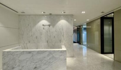 A modern office lobby with marble floors, a marble reception desk, and glass-walled offices along the corridor.