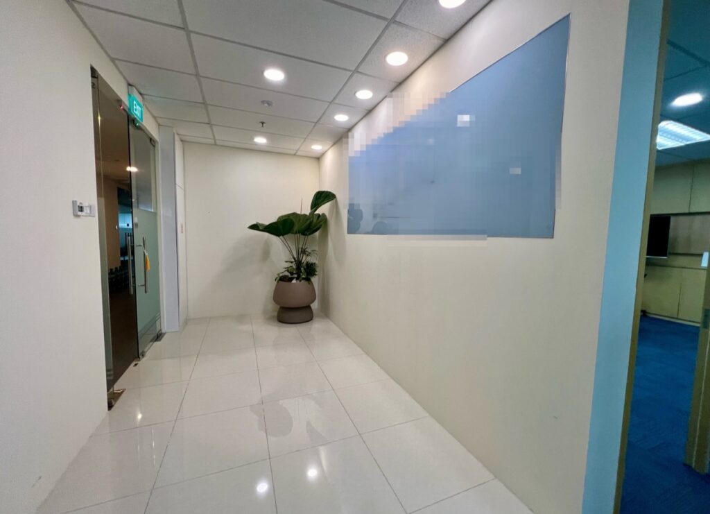 A clean, well-lit office corridor with white walls, tiled floor, a glass door on the left, a potted plant, and a large frosted glass panel on the right wall.