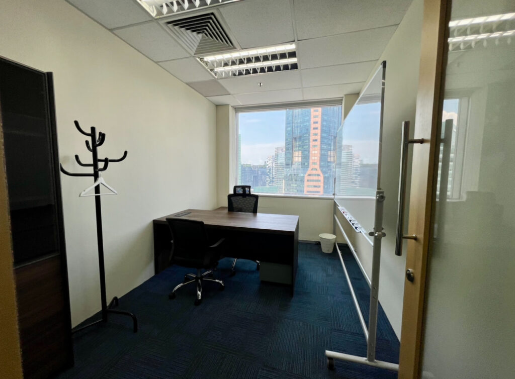 A small office with a desk, chair, whiteboard, coat stand, and a window showing city buildings outside.
