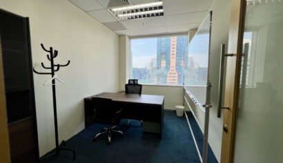 A small office with a desk, chair, whiteboard, coat stand, and a window showing city buildings outside.