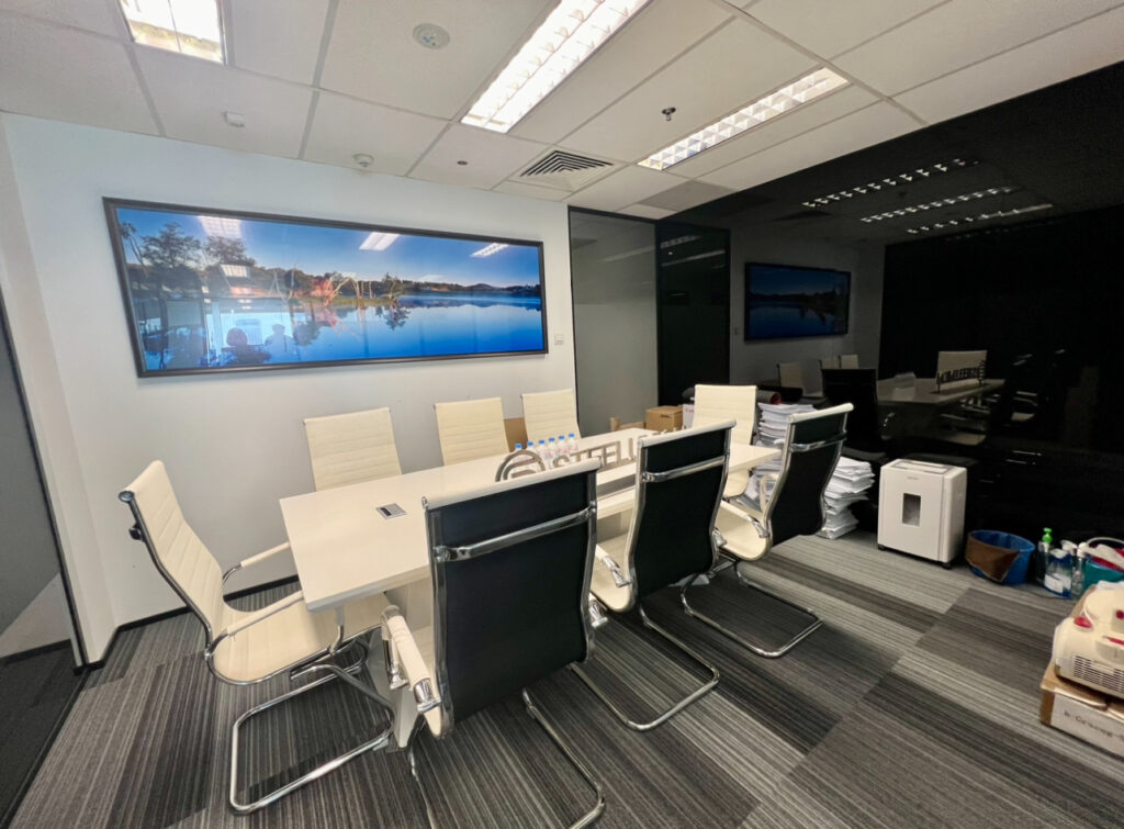 A modern conference room with a long white table, eight chairs, wall art, and office equipment placed around the room.