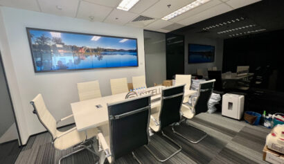 A modern conference room with a long white table, eight chairs, wall art, and office equipment placed around the room.