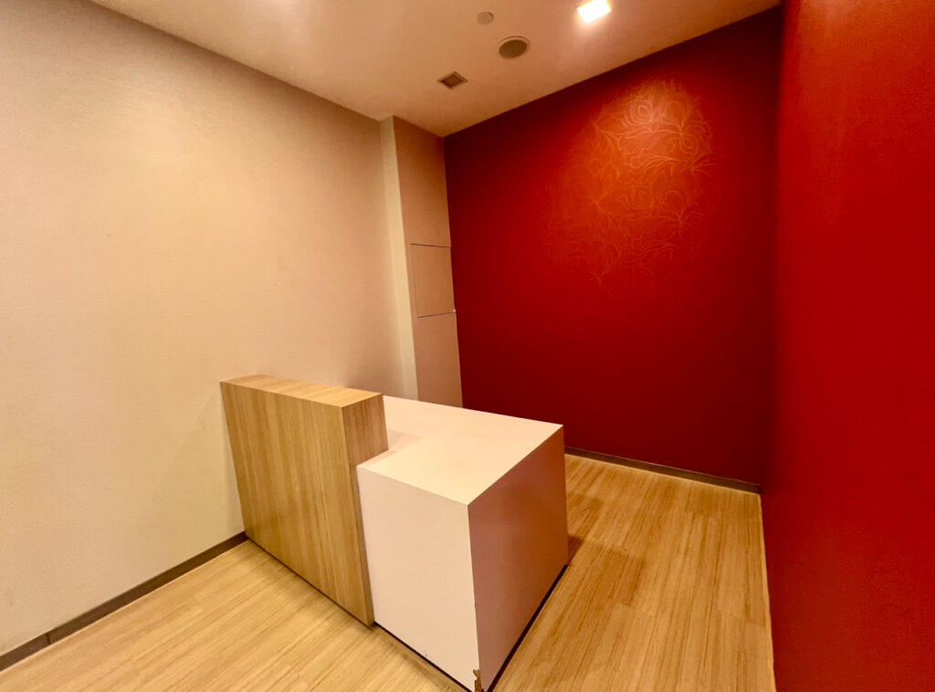 A small, empty room with red and white walls, a wooden floor, and a modern desk with wood and white finishes placed in the corner.