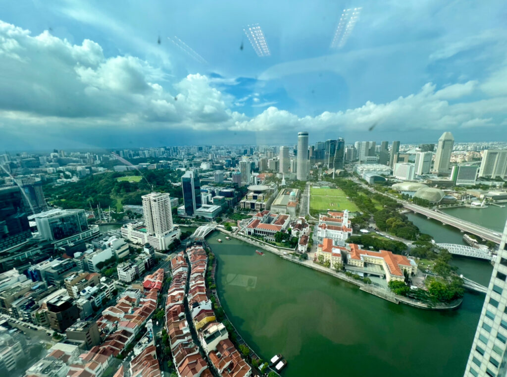 Aerial view of a city with a river running through it, high-rise buildings, a park, and densely-packed houses under a partly cloudy sky.