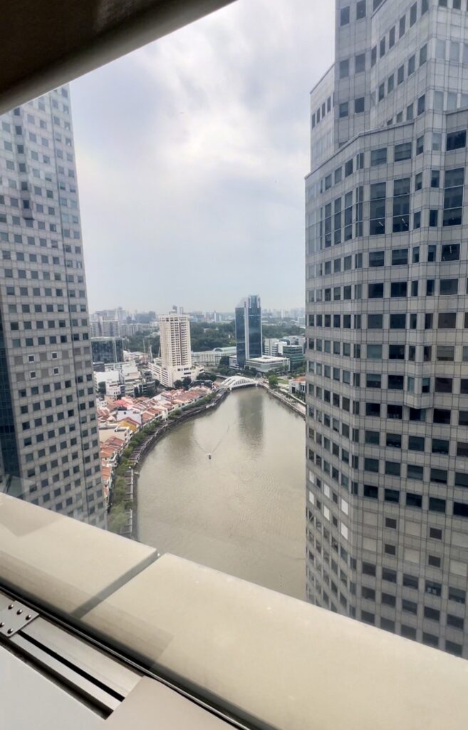 View through a window showing a river flanked by two tall office buildings, with cityscape and cloudy sky in the background.