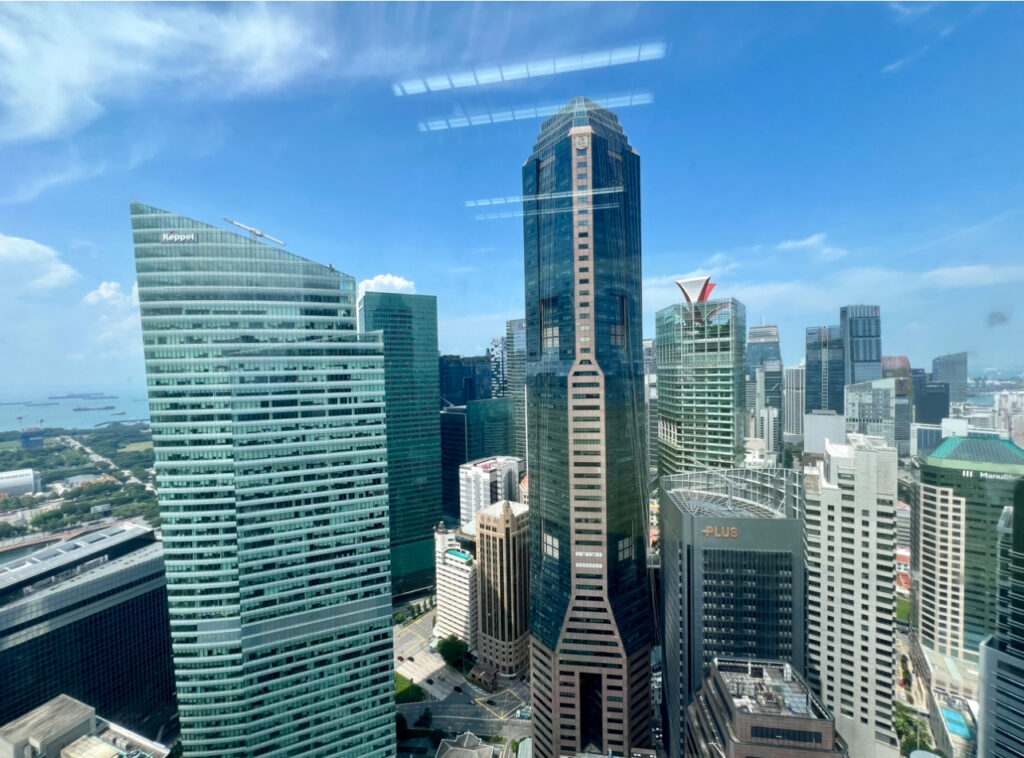 View of modern high-rise office buildings in a city’s central business district under a clear blue sky, with reflections of ceiling lights on the window.
