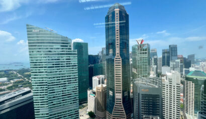 View of modern high-rise office buildings in a city’s central business district under a clear blue sky, with reflections of ceiling lights on the window.