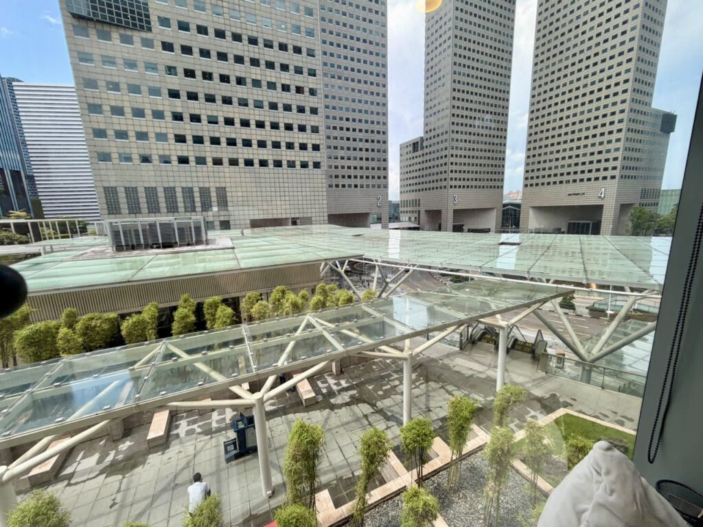View of a modern cityscape with tall office buildings, glass rooftops, and a terrace area with plants and benches.