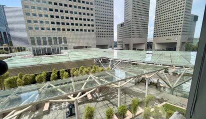 View of a modern cityscape with tall office buildings, glass rooftops, and a terrace area with plants and benches.
