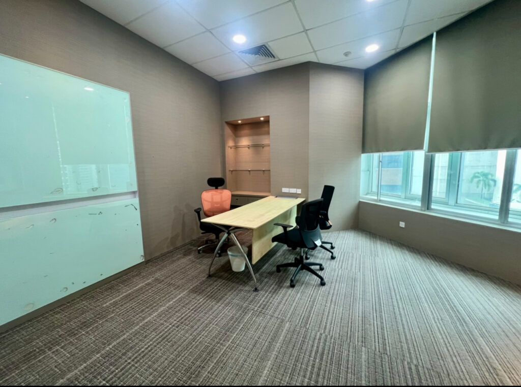 Modern office with two chairs at a wooden table, whiteboard on the wall, large windows with blinds, and carpeted floor.