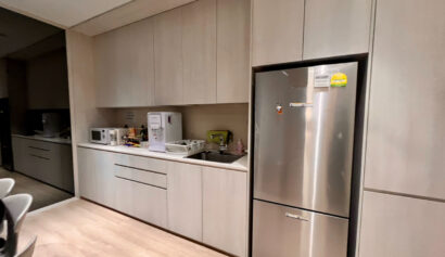 Modern kitchen with light wood cupboards, a stainless steel fridge, microwave, water dispenser, sink, and countertop appliances.