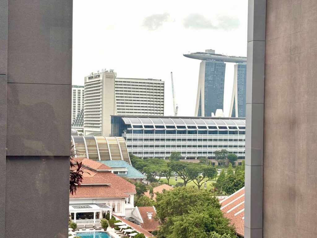 View of a cityscape featuring Marina Bay Sands hotel in the background, modern and traditional buildings, trees, and a swimming pool in the foreground.