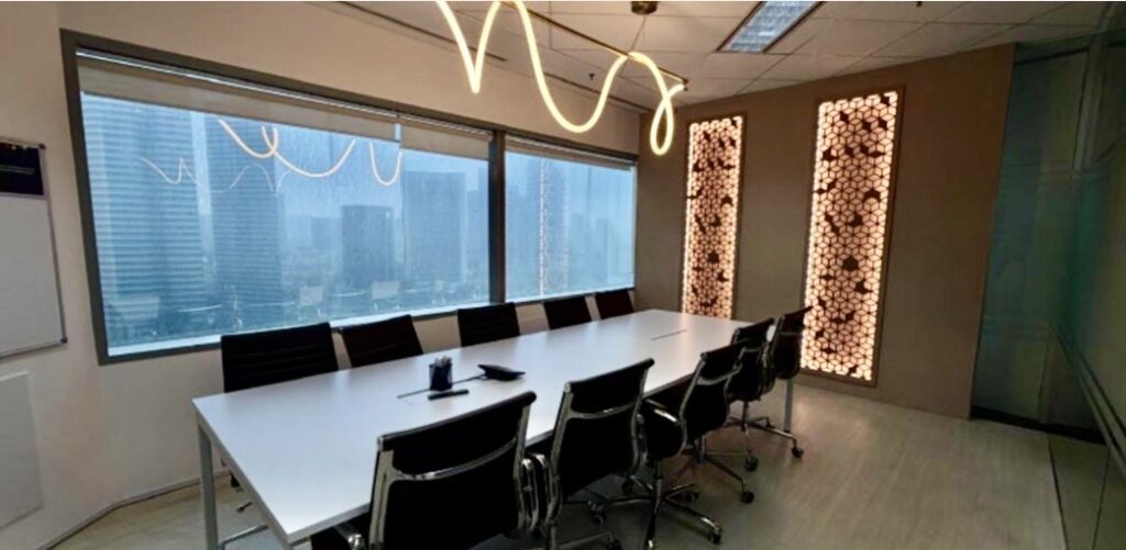Modern conference room with a long white table, black chairs, large windows showing city buildings, and decorative light panels on the wall.
