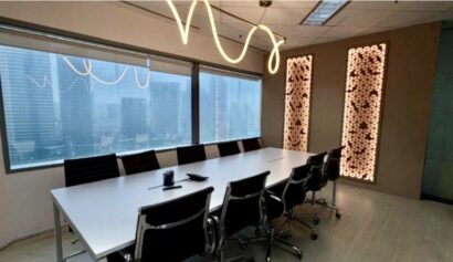 Modern conference room with a long white table, black chairs, large windows showing city buildings, and decorative light panels on the wall.