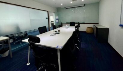Conference room with a long white table, black chairs, office supplies on the table, and glass walls.