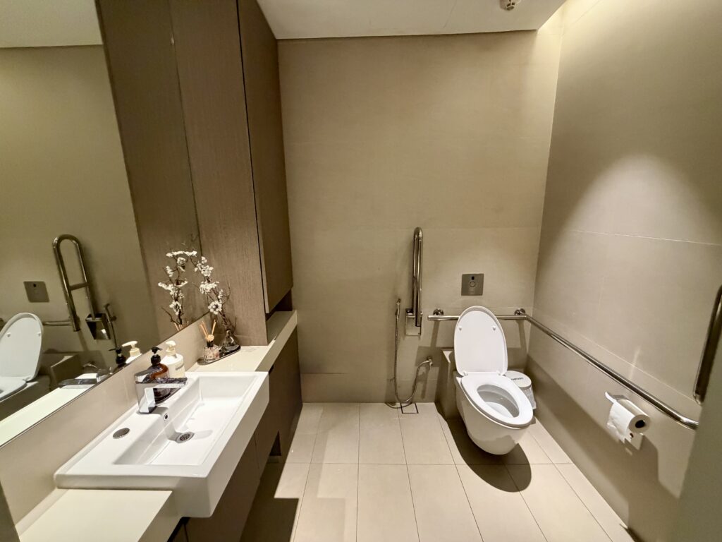 Accessible bathroom with a toilet, basin, safety grab rails, toilet roll holder, and decorative items on the sink counter.