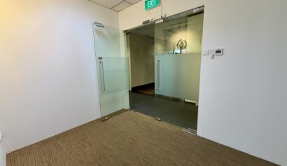 Open glass doors lead from a carpeted corridor into an office area with a visible exit sign above the doorway.