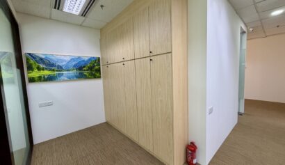 Office corridor with a large wooden cupboard, a fire extinguisher on the floor, beige carpet, and a wall-mounted nature landscape photograph.