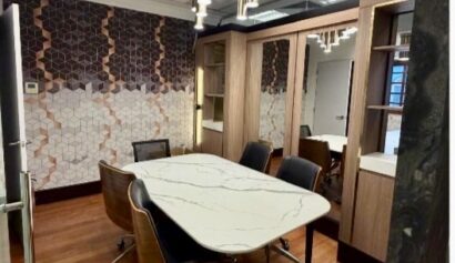 Small meeting room with a marble table, five chairs on castors, patterned feature wall, wooden flooring, and ceiling lights.