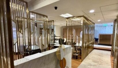 Modern office lobby with marble reception desk, gold decorative dividers, carpeted floor, and ceiling lights.