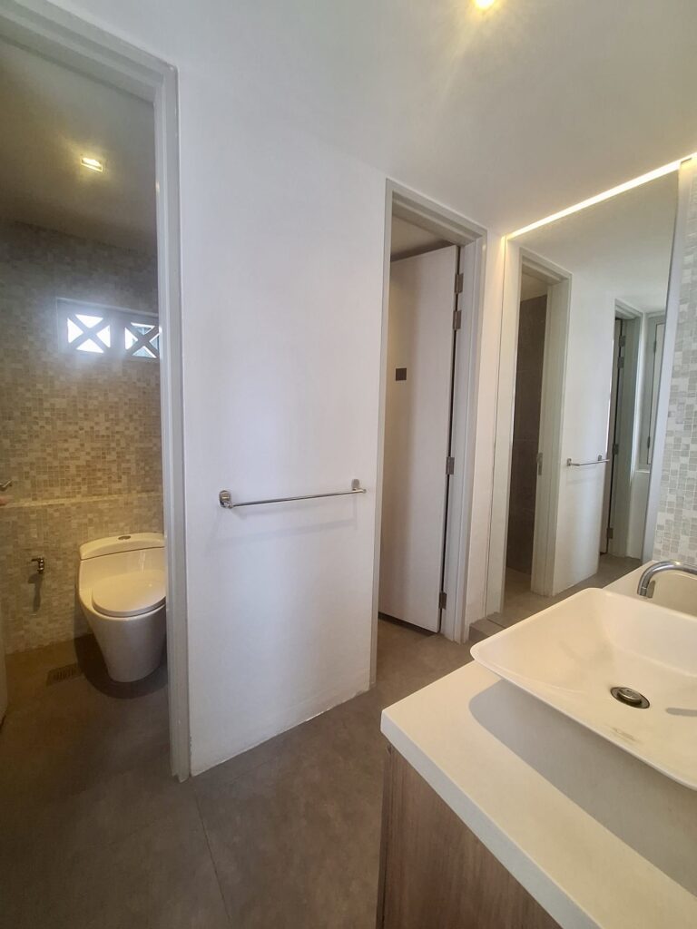 Modern bathroom with a toilet in a separate small room, a countertop basin, towel rail, and large mirror, with neutral tile and wall colours.