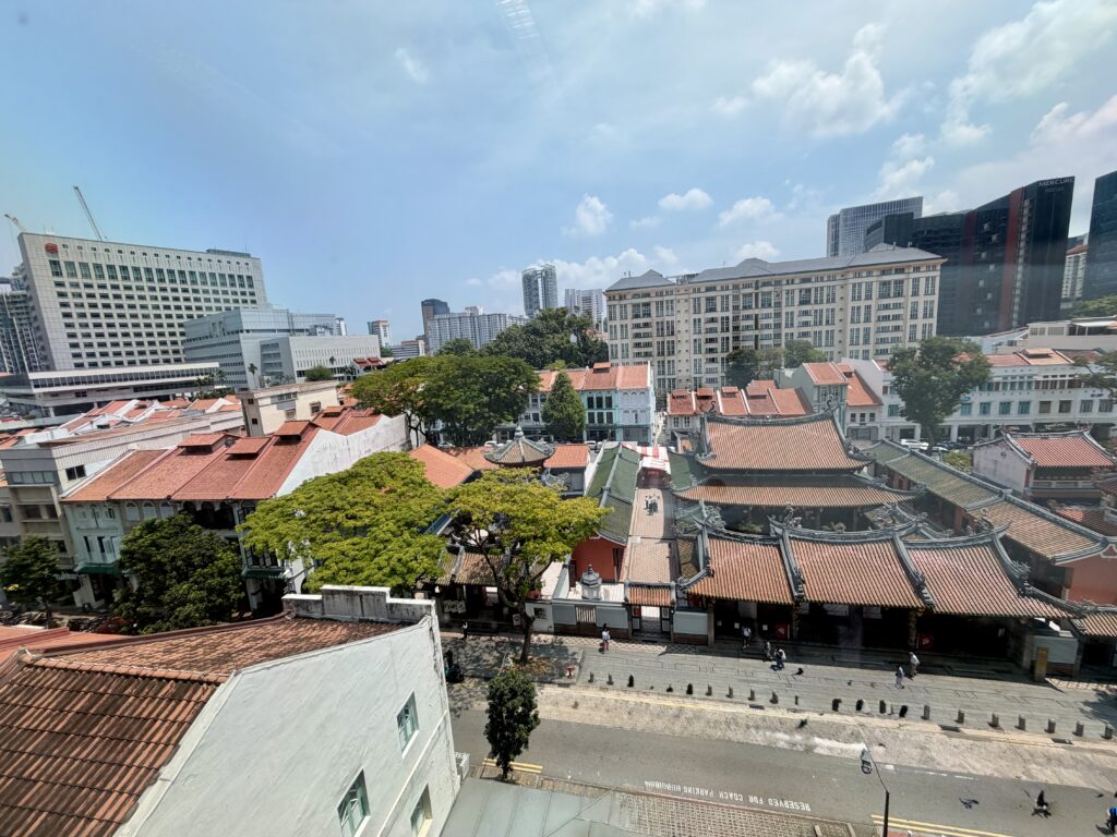 A high-angle view of the Thian Hock Keng Temple complex in Singapore, surrounded by shophouses and modern high-rise buildings under a clear blue sky.