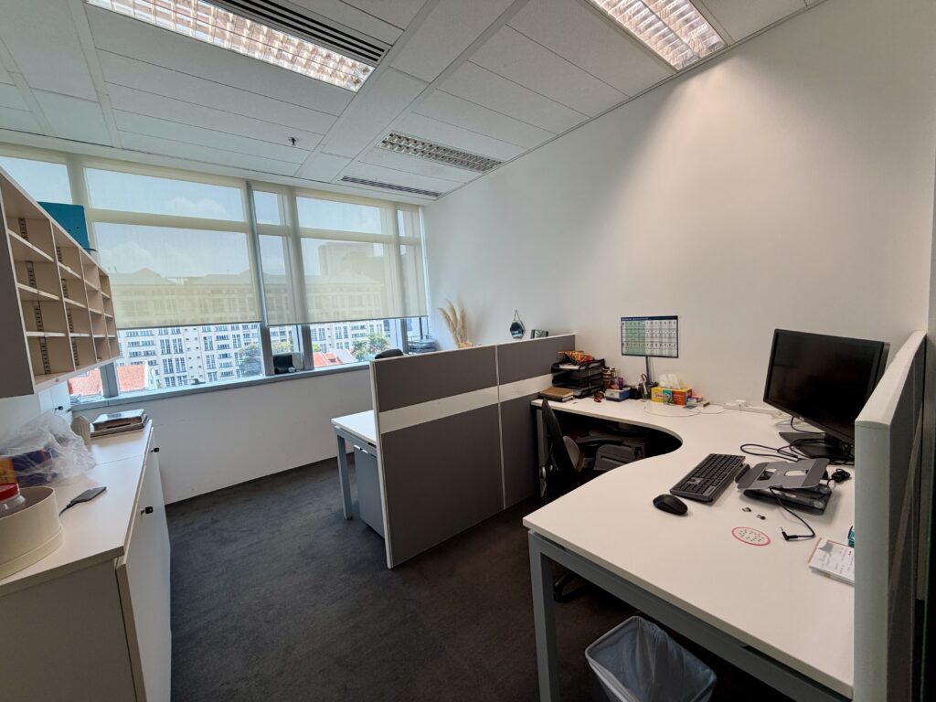 A modern office with two workstations, computers, office supplies, shelves, and a large window providing natural light and a city view.