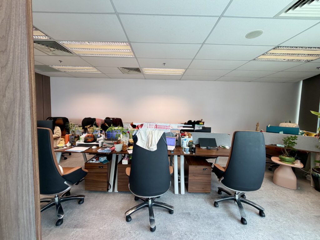Office cubicle area with three black swivel chairs facing cluttered desks.