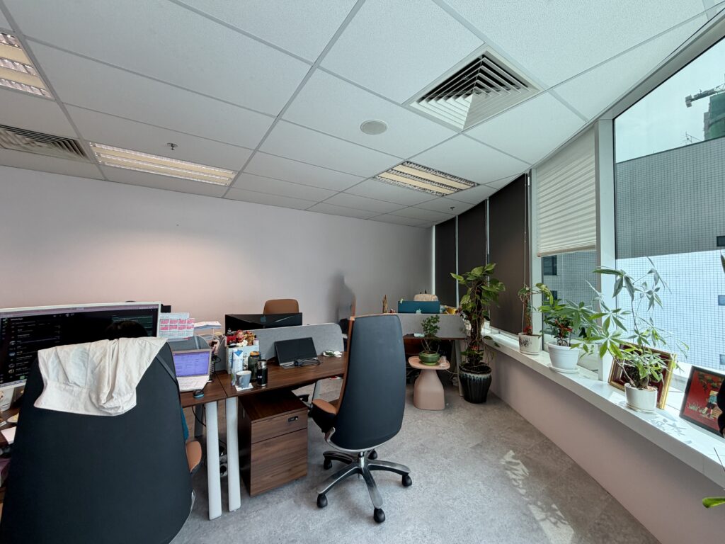 An office with two desks, swivel chairs, and several potted plants along a windowsill.