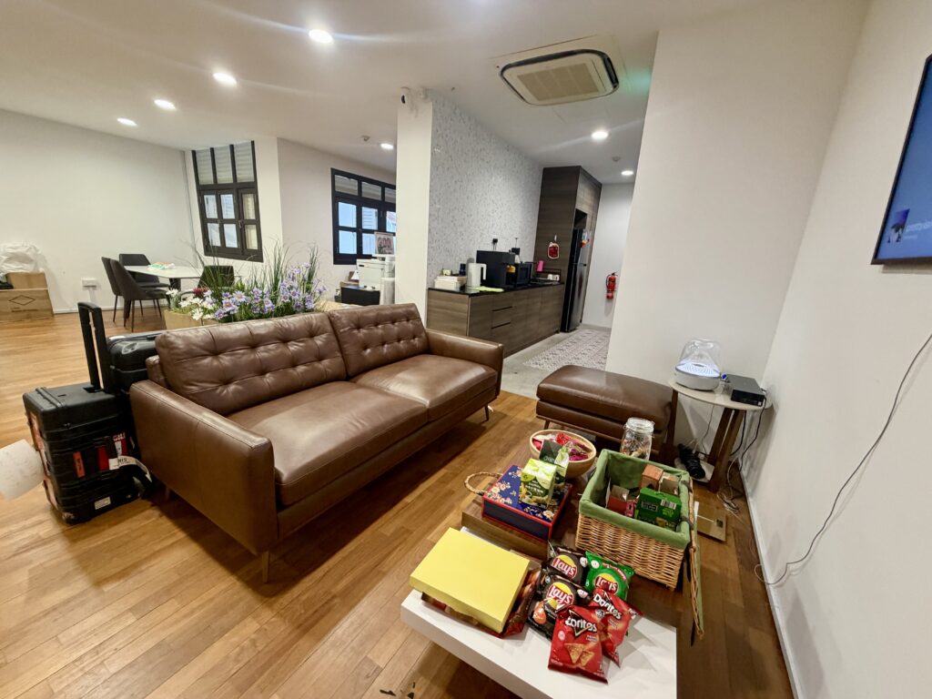 A brown leather sofa and ottoman in a lounge, with a coffee table featuring a basket of snacks and assorted boxes.