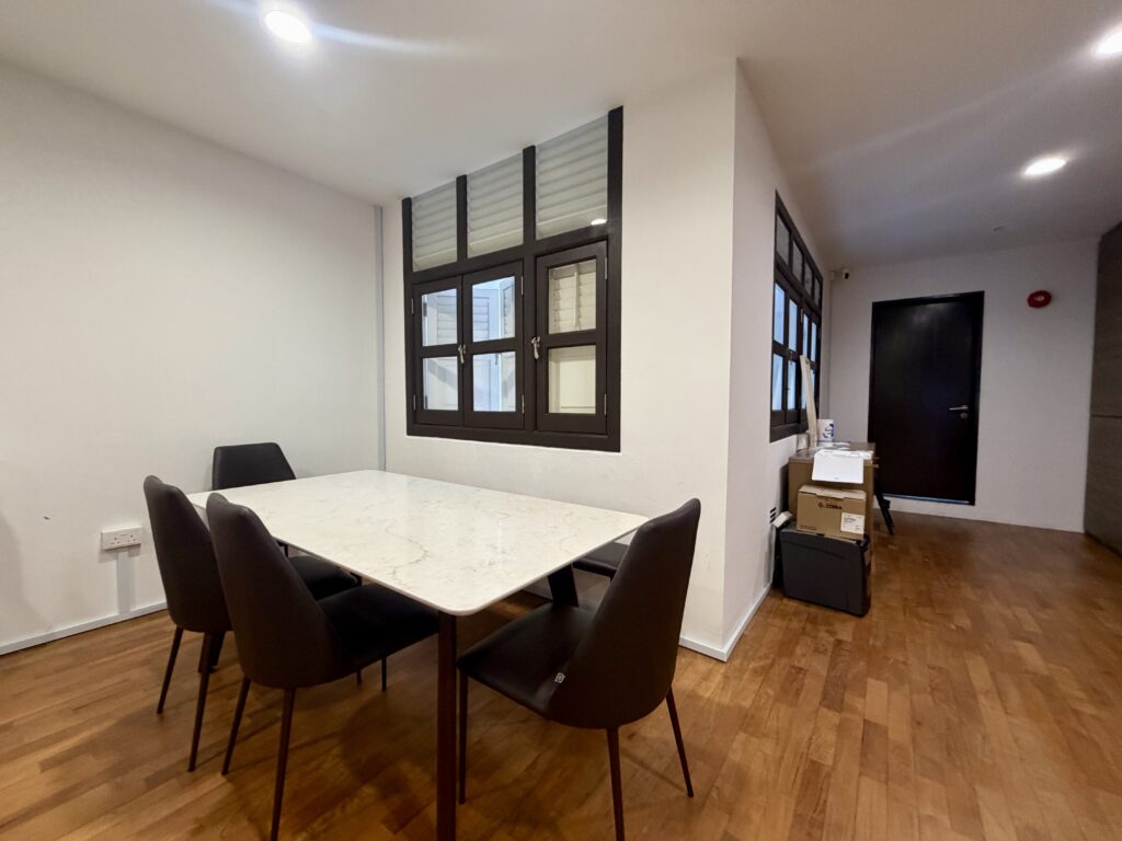 A dining table with four grey chairs in a room with wooden floors and windows with dark frames.