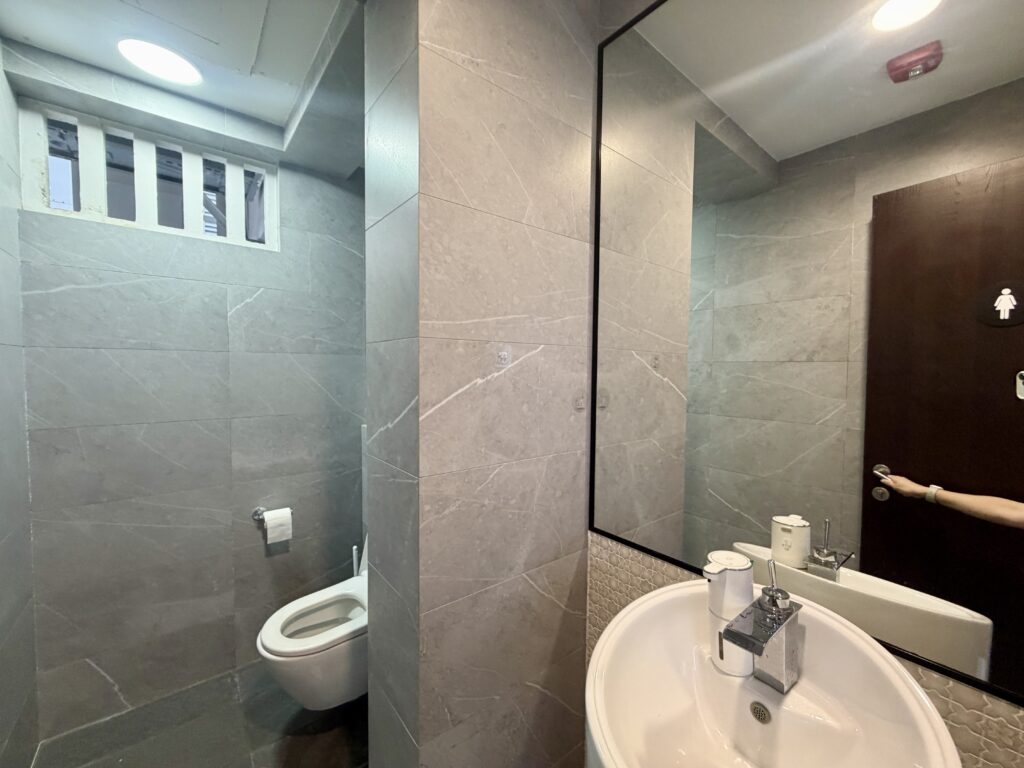 A small, tiled bathroom featuring a toilet in a recessed area and a vanity basin with a wall-mounted mirror.