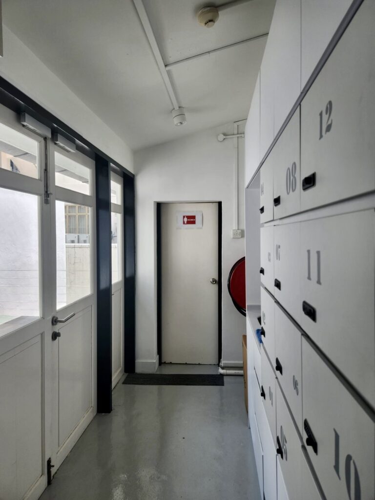 A narrow corridor with a row of numbered white storage lockers on the right and a door labelled “Women” at the end.