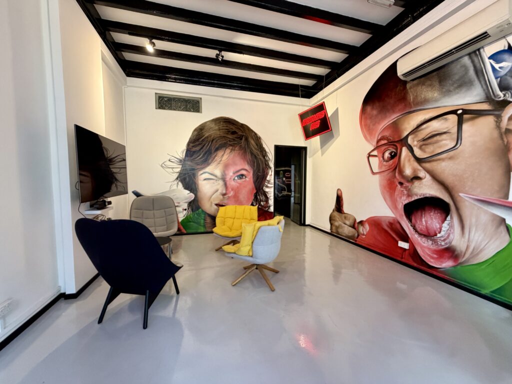 A lounge area with several chairs and a large wall mural depicting two people with expressive faces.